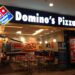 Entrance of a Domino's Pizza restaurant with signage and seating area visible.