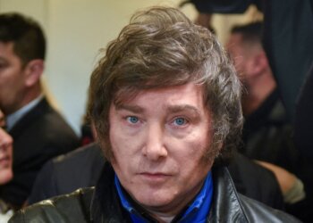 A man with dark, wavy hair and blue eyes wearing a black leather jacket.