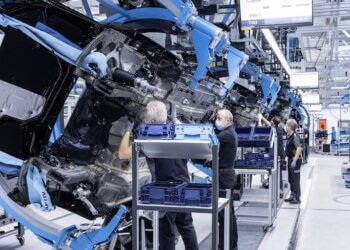Workers assembling a car chassis on an assembly line in a manufacturing facility.