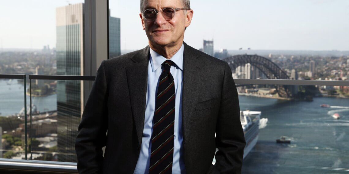 Man wearing glasses and a suit standing in front of Sydney Harbour with the Sydney Harbour Bridge in the background.