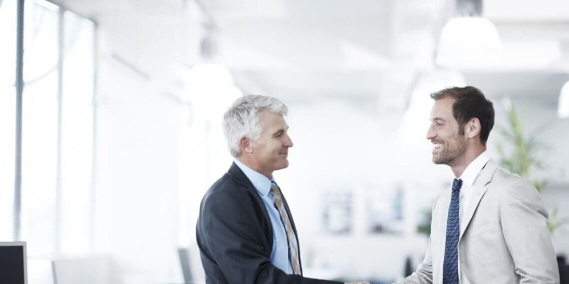Two men in business attire shaking hands in a modern office environment.