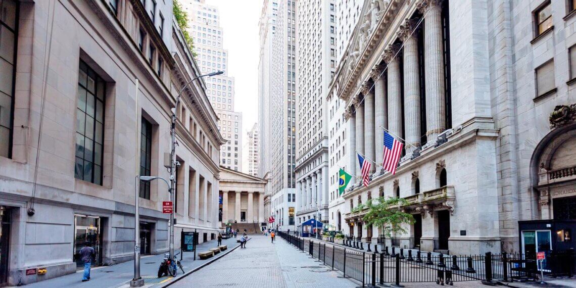 View of Wall Street featuring American flags and tall buildings on either side of the street.