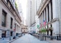 View of Wall Street featuring American flags and tall buildings on either side of the street.