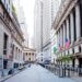 View of Wall Street featuring American flags and tall buildings on either side of the street.