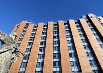 A statue of a figure with outstretched arms in front of a modern brick building with large windows.