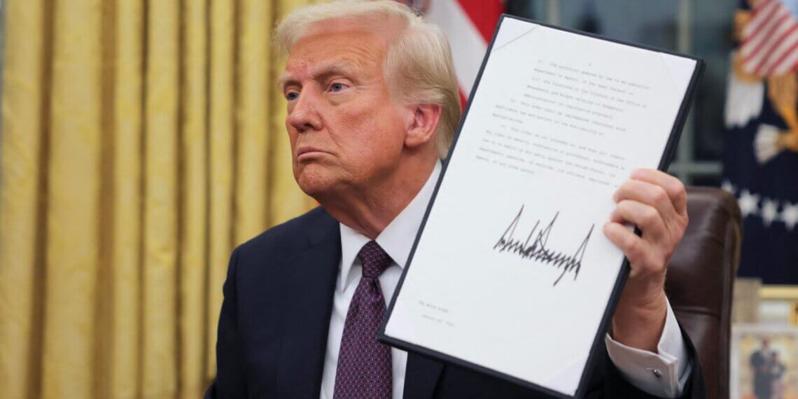 Donald Trump holding a signed document while seated in the Oval Office.