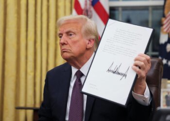 Donald Trump holding a signed document while seated in the Oval Office.