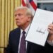 Donald Trump holding a signed document while seated in the Oval Office.