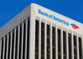 Bank of America logo displayed on the top of a tall building with a blue sky background.