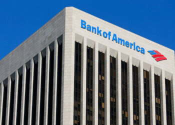 Bank of America logo displayed on the top of a tall building with a blue sky background.