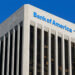 Bank of America logo displayed on the top of a tall building with a blue sky background.