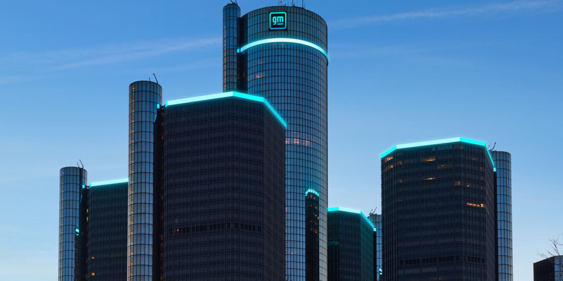 The General Motors Renaissance Center, featuring modern architecture and illuminated edges, against a blue sky.
