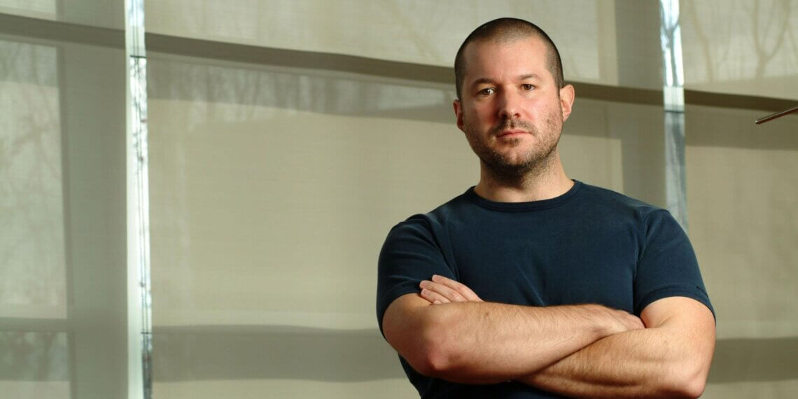 Man with short hair and a blue t-shirt standing with arms crossed in front of a light background.