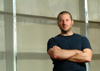 Man with short hair and a blue t-shirt standing with arms crossed in front of a light background.