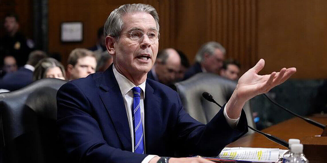 A man in a suit speaking during a Senate hearing, gesturing with his hand while seated at a table.