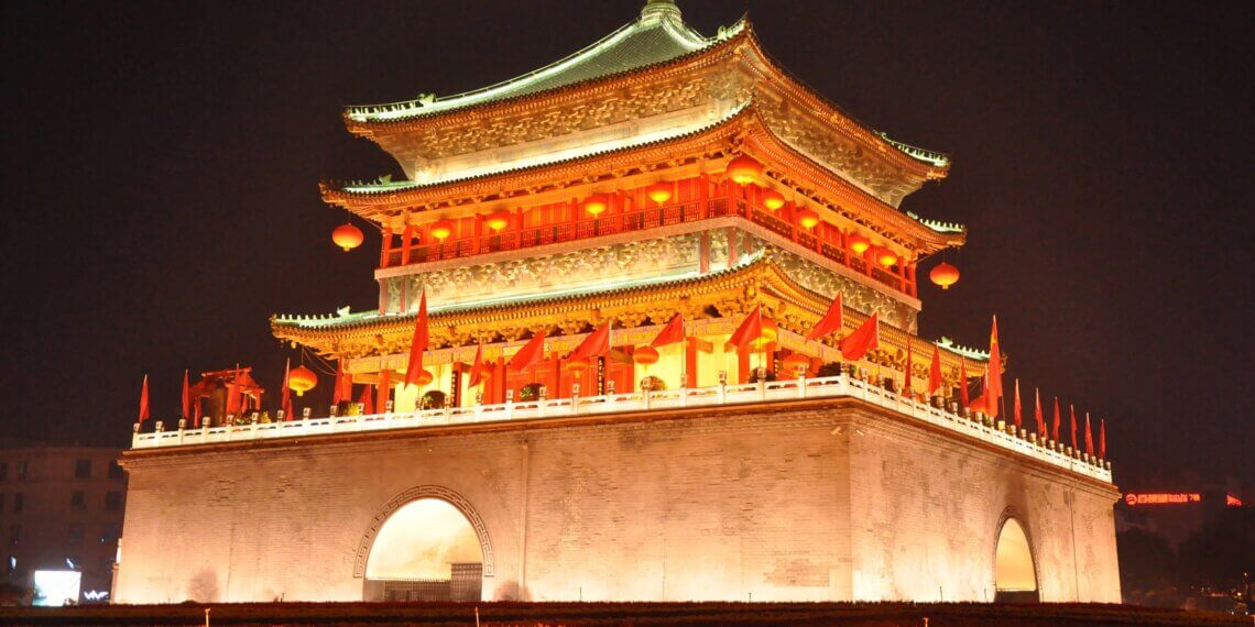 Illuminated traditional Chinese building with ornate roof and red lanterns at night.