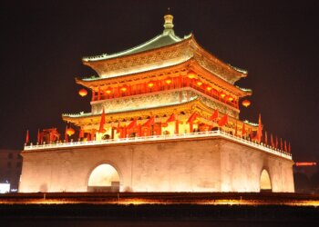 Illuminated traditional Chinese building with ornate roof and red lanterns at night.