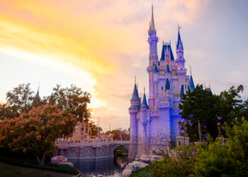 Cinderella Castle illuminated at sunset with a colorful sky in the background.