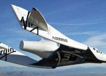 Virgin Galactic spacecraft flying in the sky with a clear blue background and mountains below.