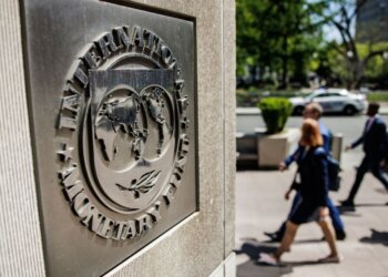 Close-up of the International Monetary Fund logo on a stone wall with people walking in the background.