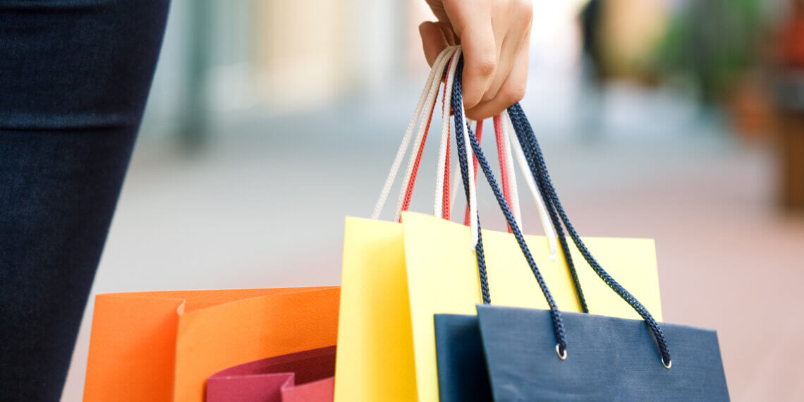 A hand holding multiple colorful shopping bags in various colors including orange, yellow, and blue.
