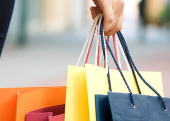 A hand holding multiple colorful shopping bags in various colors including orange, yellow, and blue.