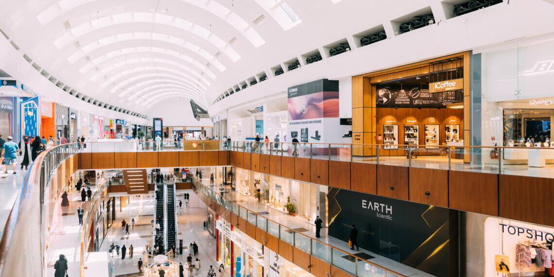 Interior view of a multi-level shopping center featuring various retail stores and shoppers.