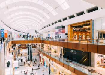 Interior view of a multi-level shopping center featuring various retail stores and shoppers.