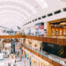 Interior view of a multi-level shopping center featuring various retail stores and shoppers.