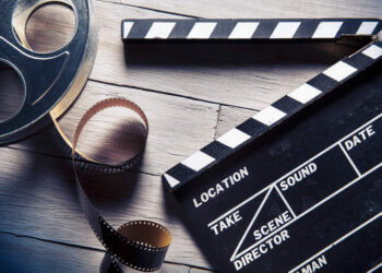A film reel and a clapperboard on a wooden surface with film strip.