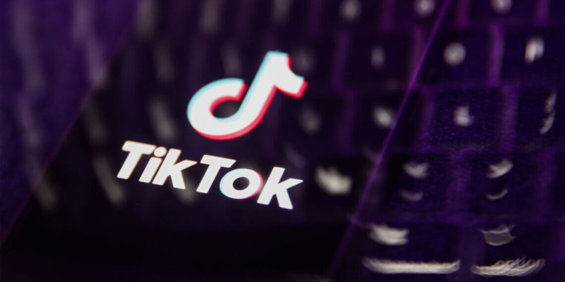 TikTok logo displayed on a blurred keyboard background with purple lighting.
