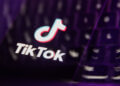 TikTok logo displayed on a blurred keyboard background with purple lighting.