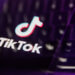 TikTok logo displayed on a blurred keyboard background with purple lighting.