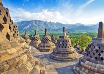 Stone stupas of Borobudur Temple with mountains in the background under a clear sky.