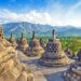 Stone stupas of Borobudur Temple with mountains in the background under a clear sky.
