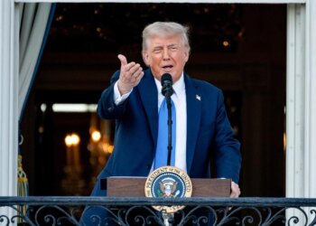 Man in a suit speaking at a podium with the Presidential seal in a formal setting.