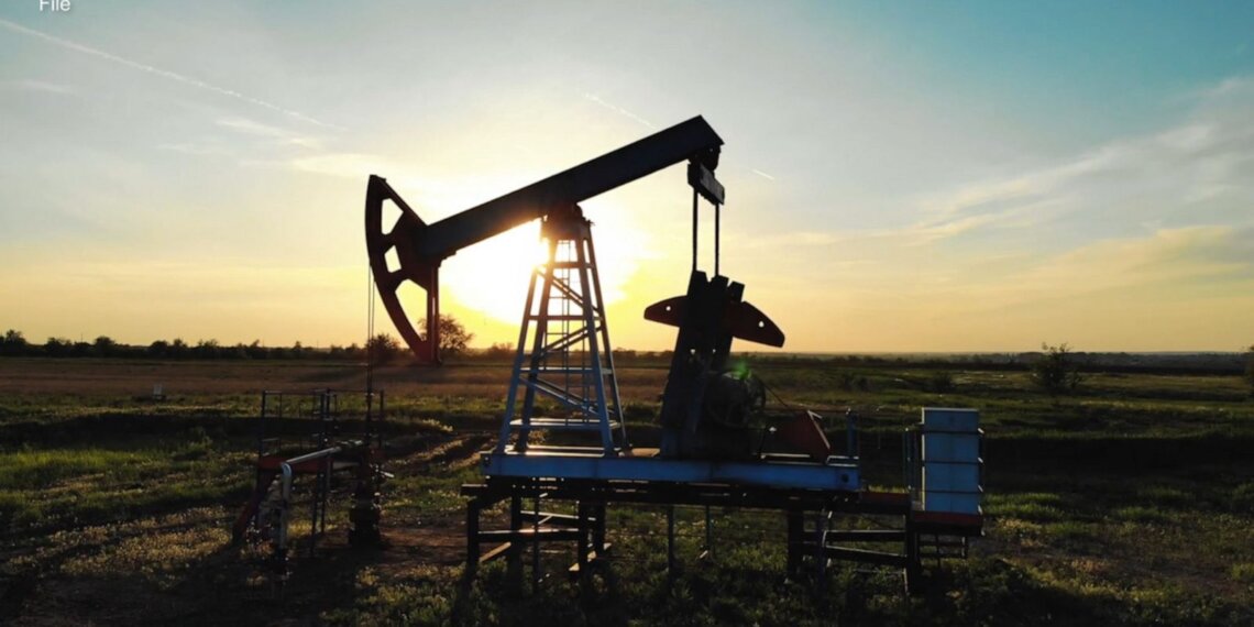 An oil pump jack silhouetted against a sunset sky in an open field.