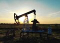 An oil pump jack silhouetted against a sunset sky in an open field.