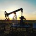 An oil pump jack silhouetted against a sunset sky in an open field.