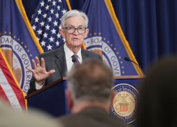 Federal Reserve Chair Jerome Powell addressing an audience during a press conference with flags in the background.
