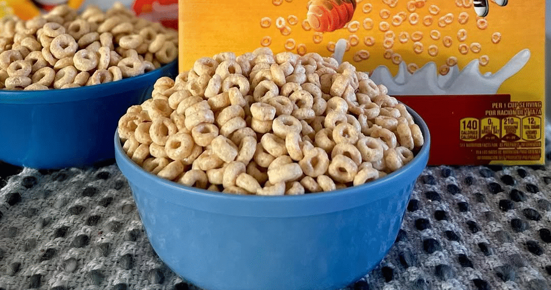 A blue bowl filled with Honey Nut Cheerios cereal on a textured surface.