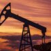Silhouette of an oil jack pump against a colorful sunset sky.
