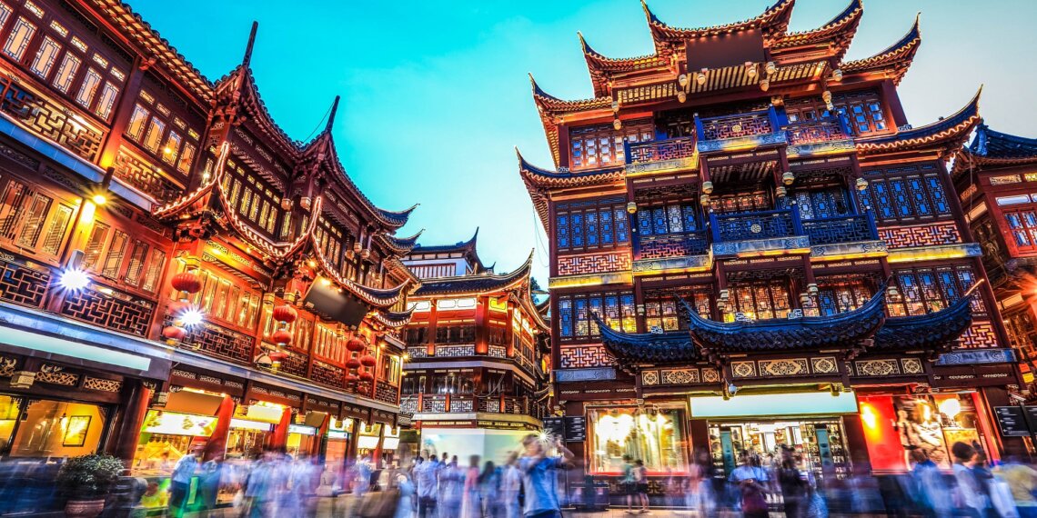 Illuminated traditional buildings in Yuyuan Garden, Shanghai, with people walking in the foreground at night.
