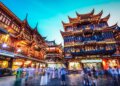 Illuminated traditional buildings in Yuyuan Garden, Shanghai, with people walking in the foreground at night.