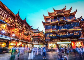 Illuminated traditional buildings in Yuyuan Garden, Shanghai, with people walking in the foreground at night.