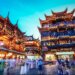 Illuminated traditional buildings in Yuyuan Garden, Shanghai, with people walking in the foreground at night.