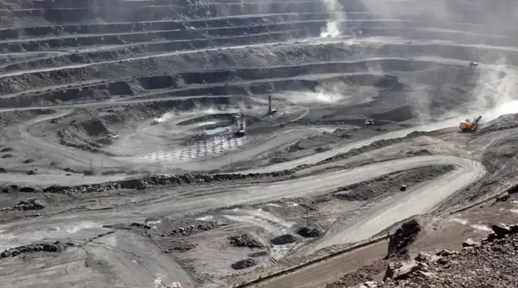 Aerial view of an open-pit mining site with machinery and layered earth formations.