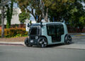A compact autonomous electric vehicle parked on a street with trees in the background.