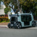 A compact autonomous electric vehicle parked on a street with trees in the background.