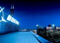 Boeing logo illuminated on a building rooftop at night with city skyline in the background.